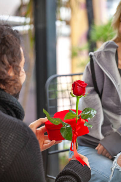 Young man hugging his girlfriend from behind and surprising her with a  red rose.