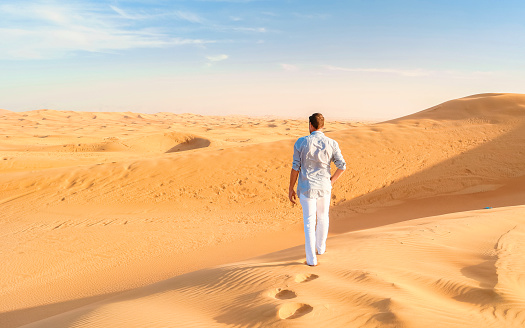Young men walking in the desert of Dubai, Sand dunes of Dubai United Arab Emirates, sand desert on a sunny afternoon in Dubai.