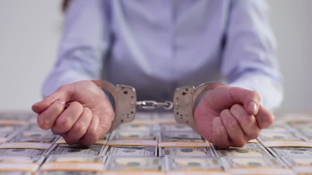 Hand of criminal in handcuffs against background of US dollars