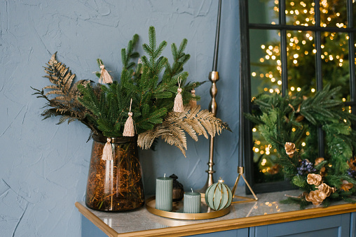 Christmas decor in the living room interior, Christmas tree branches, candles on the blue chest of drawers