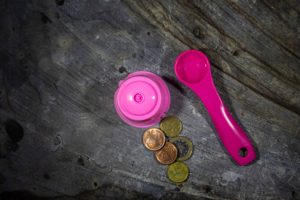 Reusable pink coffee capsule with spoon & euro coins. Sustainable brewing solution for eco-friendly coffee enthusiasts.