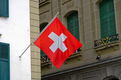 Swiss flag waving at the old town of Swiss City of Bern on a cloudy summer day. Photo taken July 1st, 2023, Bern, Switzerland.