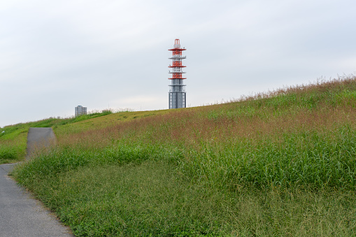 A tall communications tower on a grassy hill on an overcast morning.