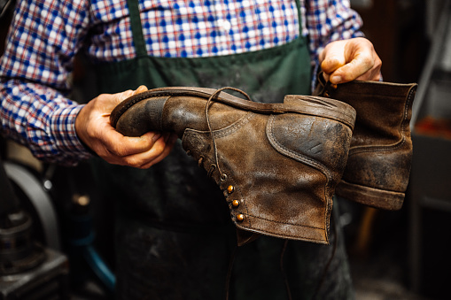 A cobbler, shoemaker, craftsman holds an old, broken shoe made of leather in his hands. Landscape format