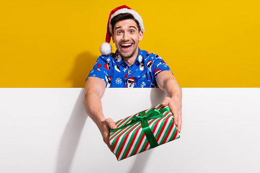 Photo of cheerful friendly guy arms hold give you x-mas giftbox empty space poster isolated on yellow color background.