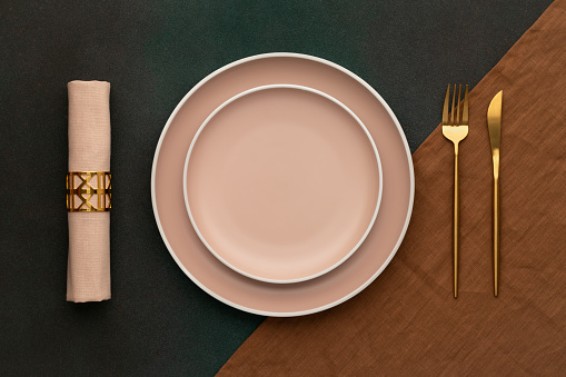 Plate with fork and knife. Gold cutlery, dark green background. Top view. Celebration place setting, brown tablecloth, fabric napkin. Dining table in luxury restaurant. Menu template, flat lay design