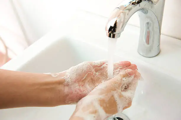 Washing of hands with soap under running water.