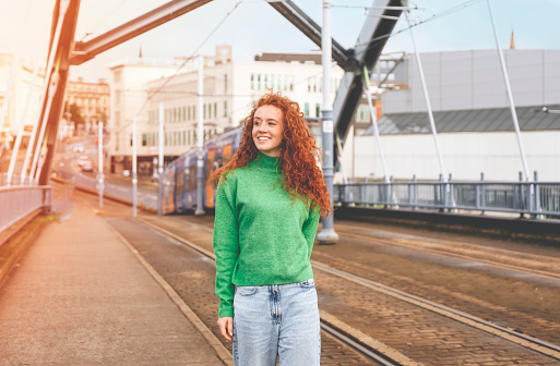 Portrait of a young happy woman with red curly hair exploring the city