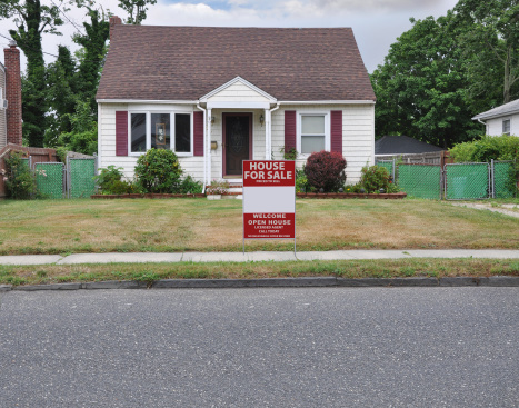 Bungalow style home with for sale sign on front yard lawn dried burnt grass.