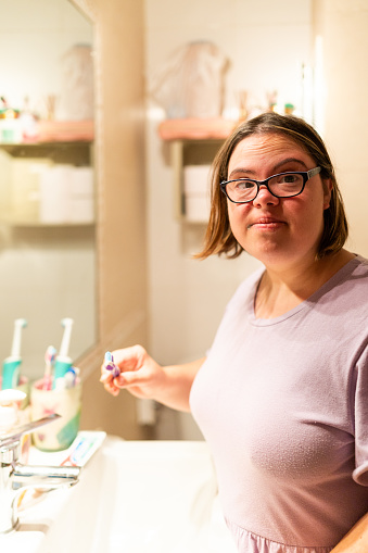 Vertical photo of a cute young woman with special needs brushing her teeth at home