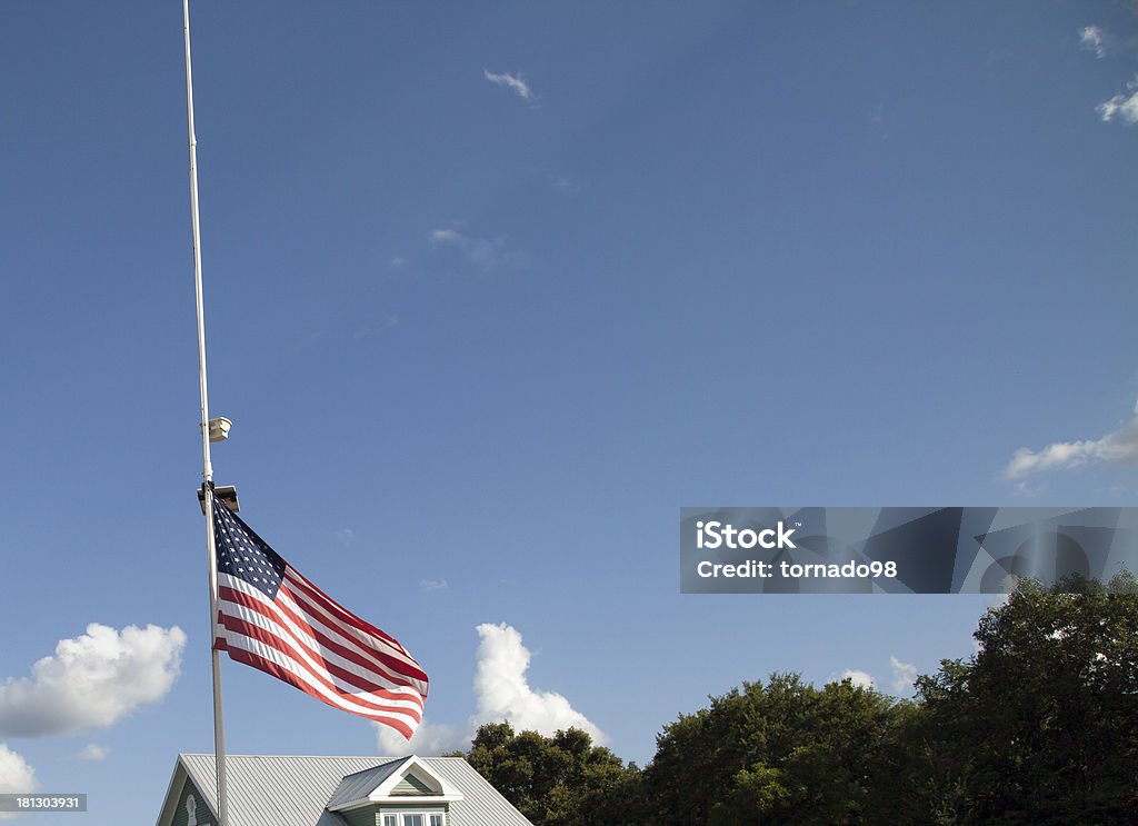American Flag at Half Mast American flag at half mast with top of house and tree tops in the background American Culture Stock Photo