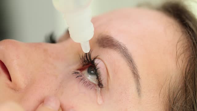 Closeup of medical drops from bottle dripping into woman eye