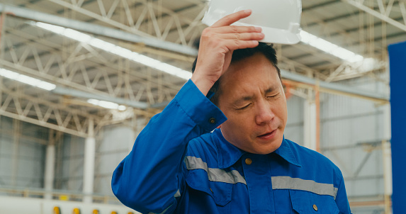 Professional Asian male industrial engineers tired take off helmet in manufacturing factory. Working in manufacturing plant or production plant concept.