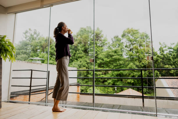 istock Contemplative mature woman drinking coffee while looking through the window  at home 1813069356