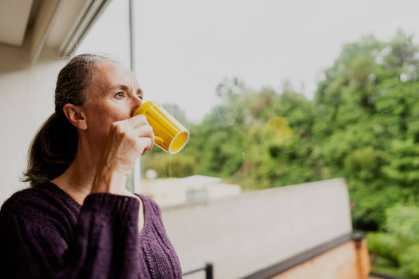 istock Contemplative mature woman drinking coffee while looking through the window  at home 1813069357
