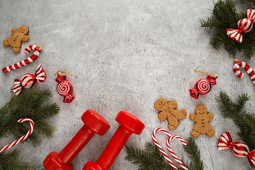 Dumbbells, Christmas tree branches, gingerbread man cookies, candy canes, ornaments and pendant decorations. Healthy fitness lifestyle flat lay composition with copy space. Seasonal fit diet choice, staying in shape during winter holiday season. Festive gym workout and sport training concept. Cheat day temptation vs dieting.
