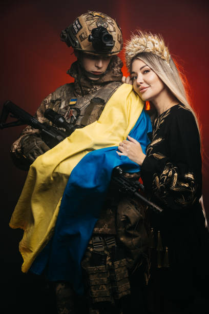 un couple amoureux à l’aube lors d’une bataille dans la fumée tient le drapeau de l’ukraine dans leurs mains. le concept d’amour invincible, la victoire de l’ukraine sur l’invasion russe. vêtements nationaux ukrainiens. - military armed forces patriotism flag photos et images de collection