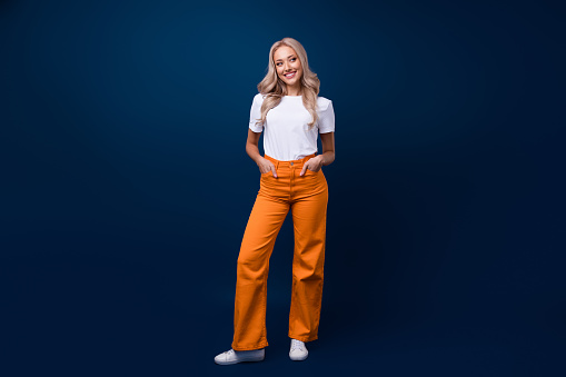 Full length photo of gorgeous pretty good mood girl hands in pockets looking empty space isolated on dark blue color background.