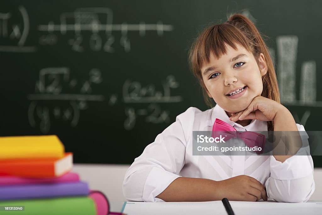 Linda pequeña niña en edad escolar sesión en el aula con sus libros - Foto de stock de Alegre libre de derechos