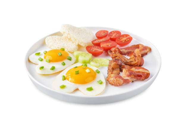 istock Fresh breakfast with fried eggs, fried bacon slices, bread slices and vegetables in the form of heart for Valentine's day holiday on a white isolated background 1813151357