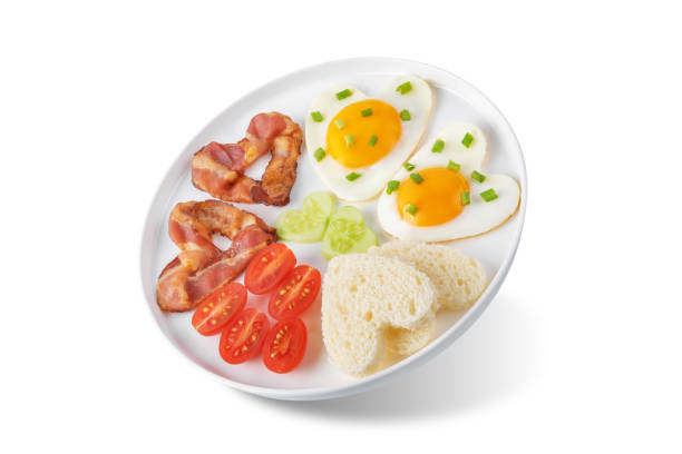 istock Fresh breakfast with fried eggs, fried bacon slices, bread slices and vegetables in the form of heart for Valentine's day holiday on a white isolated background 1813151631