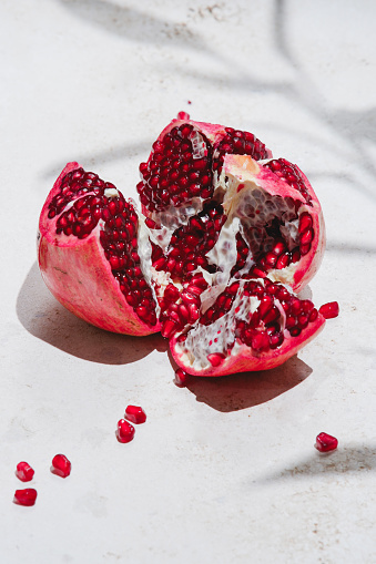 Ripe tasty red pomegranate fruit and pomegranate pieces with leaves on a light concrete background. top view