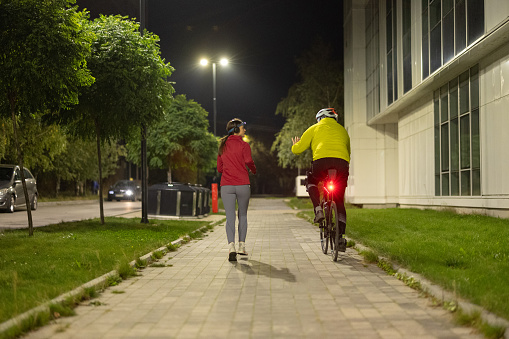 Rear view of man riding a bicycle while woman running next to him in the city at night