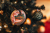 Festive shiny Christmas ball with the image of a dragon hanging on a Christmas tree with golden garland lights.