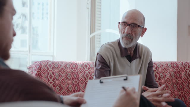 Senior Man Talking to Therapist Writing Down Notes on Clipboard