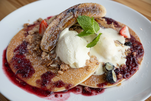 Pancake served with caramelised banana, strawberry sauce, granola and vanilla ice cream.