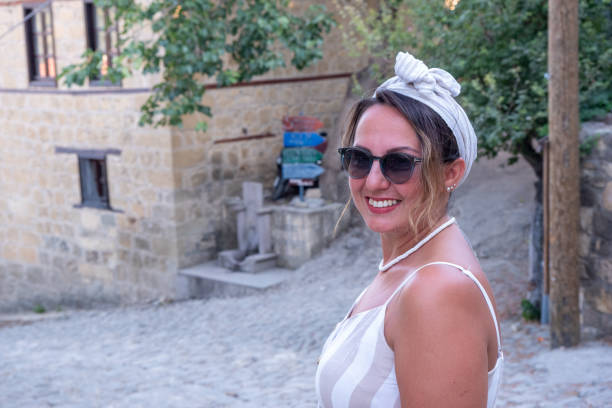 During summer, a positive middle-aged woman smiles directly at the camera, radiating warmth and cheerfulness.