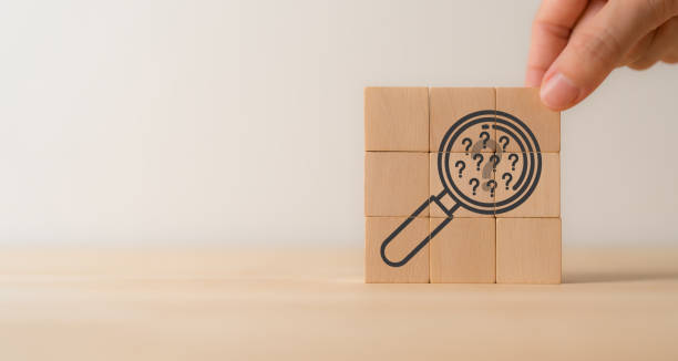 Magnifying glass, many question mark icons on wooden cube blocks. Question mark, problems and root cause analysis concept. Define problems to find solution. Finding answers, trends, opportunities.