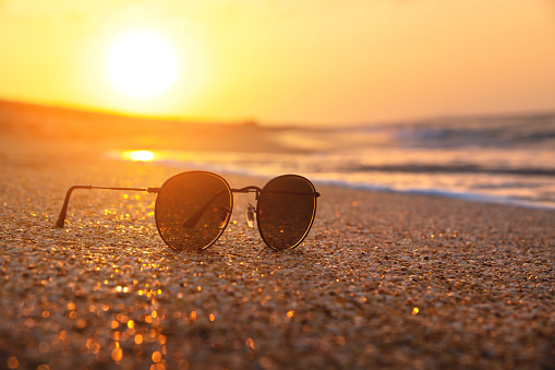 Stylish round sunglasses lie on the wet sand of the sea beach in the rays of the setting sun. Sunset and sunglasses. Sea holiday concept.