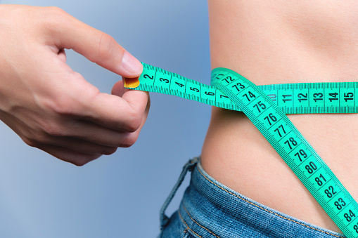 A woman measures her waist with a tape measure. Diet and body weight control concept, close-up, toned. A girl in jeans takes measurements of her figure and weight loss