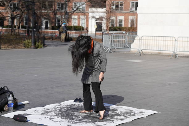 An artist in NYC paints with black paint using only her bare feet while whirling wildly to techno music on a sunny day in the village.