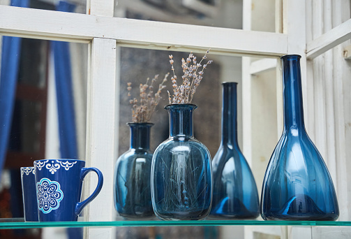 A blue glass vase with a dry plant is on the shelf. Next to it is a jug of the same material and a porcelain mug. Oriental decor.