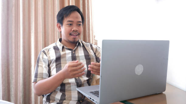 mężczyzna z azji południowo-wschodniej wyjaśnia za pośrednictwem połączenia wideo online ze swoim laptopem - southeast asian ethnicity men laptop image type zdjęcia i obrazy z banku zdjęć