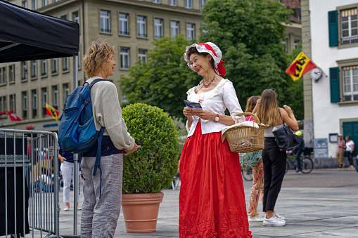 Senior woman with historic baroque costume doing promotion at Swiss capital of Bern at Federal Palace Square on a cloudy summer day. Photo taken July 1st, 2023, Bern, Switzerland.