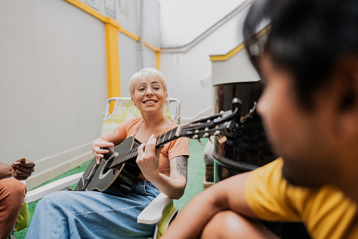 Mid adult woman playing guitar with her friends at hostel