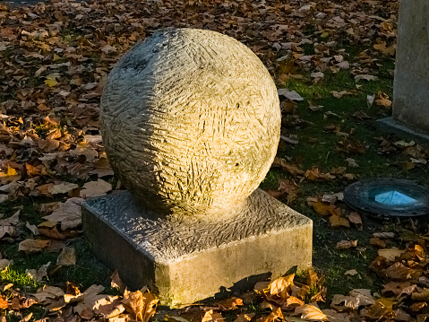 A sculpture in the form of a ball on a square pedestal in a city park. The play of light on the surface of the ball.