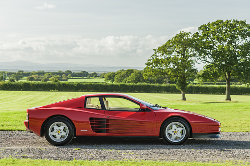 Chester, Cheshire, England, September 29th 2023. Side profile of a red Ferrari Testarossa against a field in the background.
