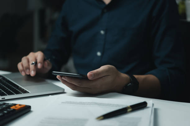 istock Businessman hand holding mobile smartphone on a table with a laptop at office... 1813255779