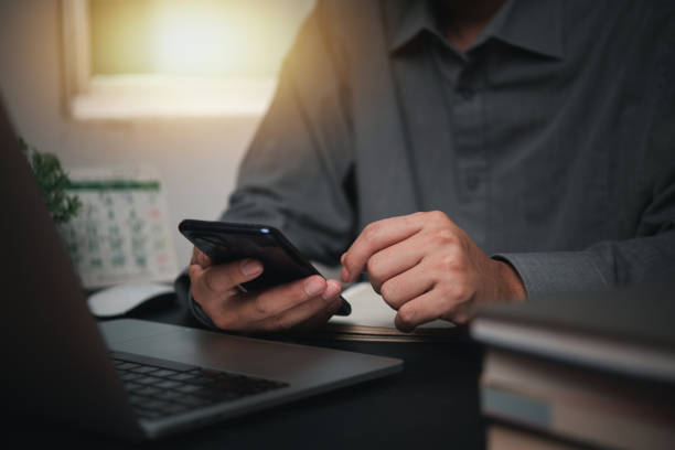 istock Businessman hand holding mobile smartphone on a table with a laptop at office.. 1813255810