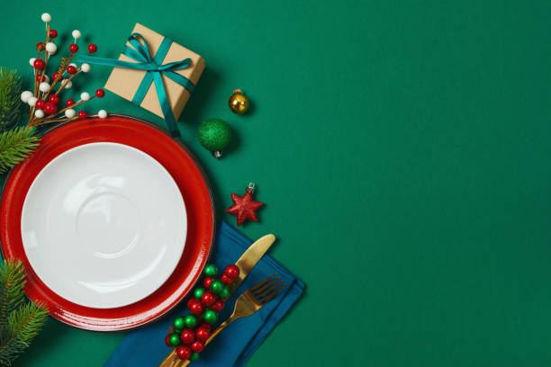 istock Christmas table decoration with plate, gift box and ornaments on green background. Elegant template for holiday card, invitation and design 1813256247
