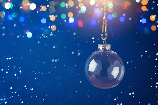 Christmas holiday background with transparent bauble ornament over festive bokeh lights