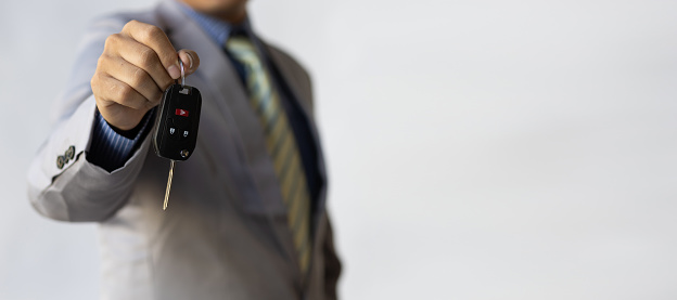 Businessman holding car keys is handing over.