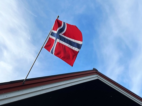 Norwegian flag on pole fixed on roof against blue sky