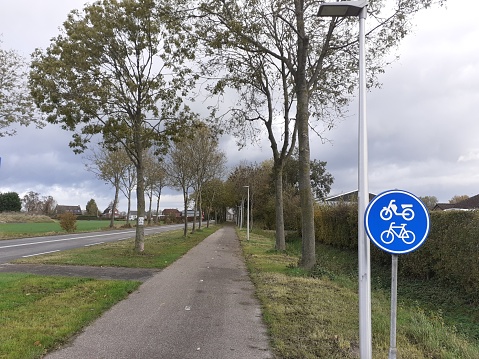 Hulst, Holland - nov 11, 2023: a separate bicycle lane with a soft shoulder and a road sign and trees next to a country road in the dutch countryside