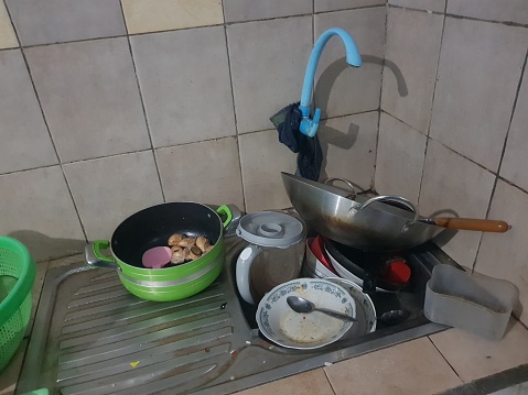 Sink full of dirty dishes with plate, fork, spoon and pan