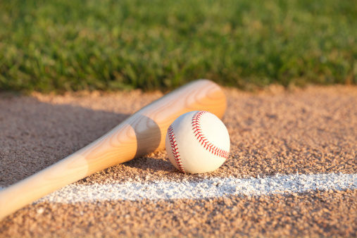 Selective focus view of a baseball and bat laying on a basepath near the infield grass